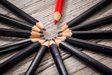 Red pencil stands out from the crowd of black  on a wooden white background.