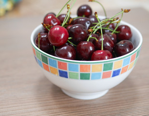 Cherries in colorful bowl on wooden surface