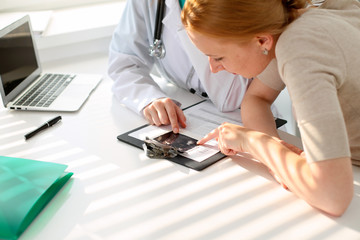 Naklejka premium Doctor pointing into medical history form and discussing something with her patient. Close-up.