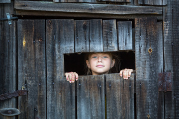 Little girl peeping from the window of the rustic barn.