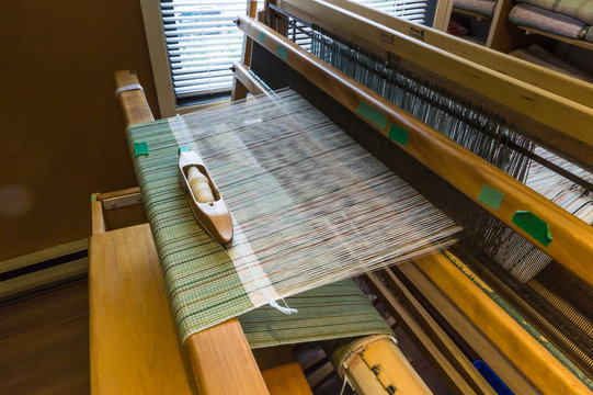  Cloth being  woven on a wooden  loom,  holding the warp threads in place while weft, filling, threads are woven through them creating a green pattern 
