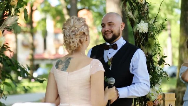 Beautiful back of bride holding a microphone telling her oath, handsome groom kissing her