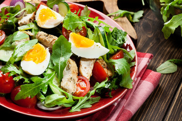 Fresh salad with chicken, tomatoes, eggs and arugula on plate