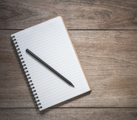 Top view of white book and black pencil on old wooden plank