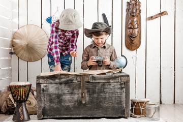 two little children in hats watching map on big old chest