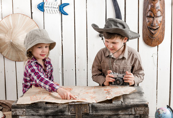 two little children in hats watching map on big old chest
