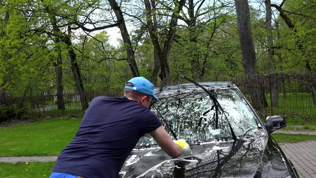 Male worker washing automobile in open air. Handheld shot.