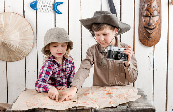 two little children in hats watching map on big old chest