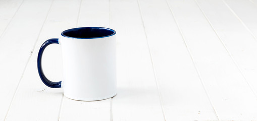 Fototapeta na wymiar white cup with dark blue handle and inside on white wooden surface