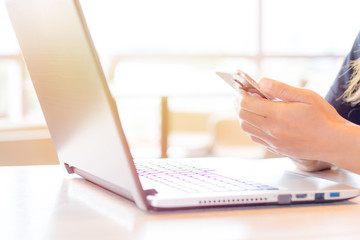 Close Up of woman's hands using mobile phone and laptop computer with blank copy space screen for your advertising text message or content, in the morning light.