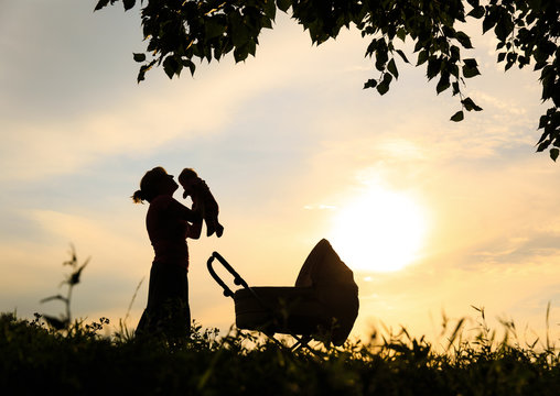 Silhouette of mother with little baby and stroller at sky