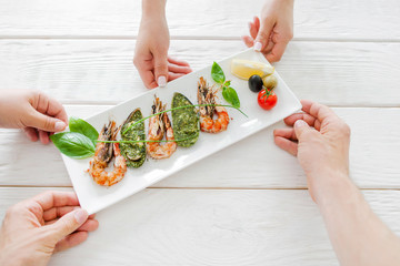 Company dining at restaurant, mediterranean cuisine. Hands of group of people sharing plate with prepared seafood mix