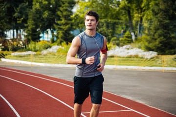 Obraz premium Young sports man running down stadium track with earphones