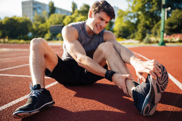 Young male runner suffering from leg cramp on the track