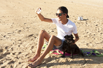 man with dog at the beach pulling a picture with the mobile phone. Sunset warm light summer