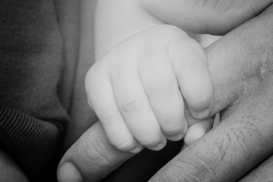 Baby's hand holding the hands of his father.