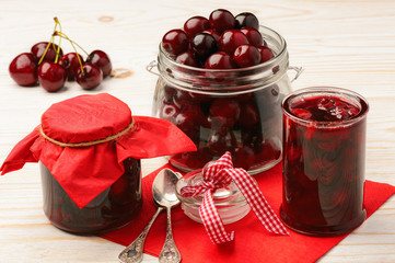 Cherry jam in glass jars on wooden background.