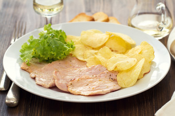fried meat with potato chips and fresh salad on white dish on brown wooden background