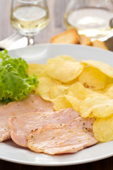 fried meat with potato chips and fresh salad on white dish on brown background