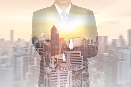 Double exposure of business man arms crossed, cityscape and sunset  as vision of leader concept.
