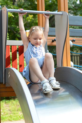 Fototapeta na wymiar Happy blond girl having fun and sliding on outdoor playground
