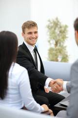 Two happy young men shaking hands while sitting at the office