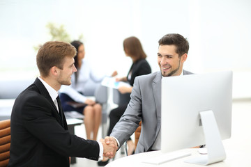 Fototapeta premium Two happy young men shaking hands while sitting at the office