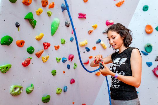 Portrait of beautiful woman rock climber belaying another climber with rope. Indoors artificial climbing wall and equipment.