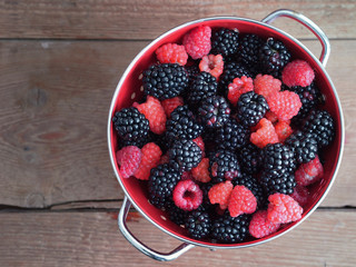 Blackberries and raspberries in bowl on wooden background. Top v