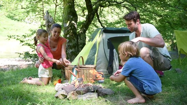 Family camping and cooking sausages in campfire