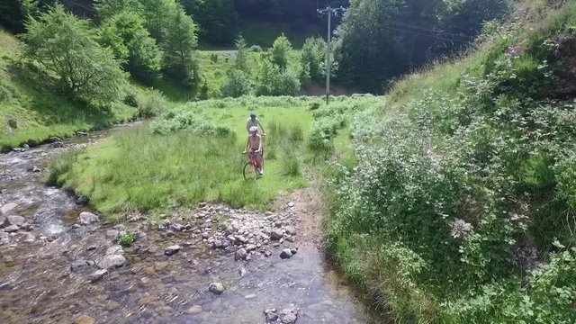 Couple crossing river stream in mountains with bikes
