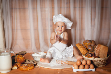 Happy baby baker sitting surrounded by bread and pastries