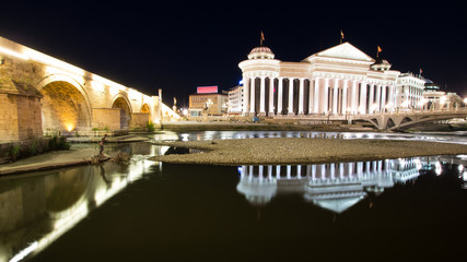 Reflections of the Archaeological Museum and the old stone bridge in the river Vardar during the night in Skopje Macedonia