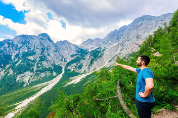 Male hiker enjoys exploring meadow landscape of European alps on cloudy day, summertime