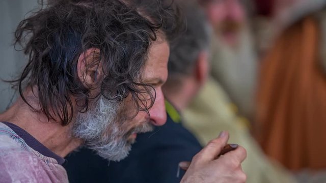 A servant is sitting at a table with a royal family and he is eating soup. He is taking a few spoons. Close-up shot.
