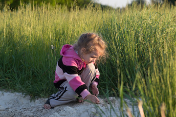 Hunkering little girl playing in field dirt outdoors at natural green meadow grass backdrop