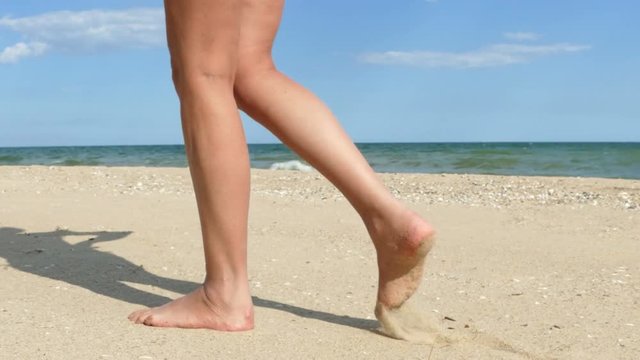 4K. Female legs go on   sea beach