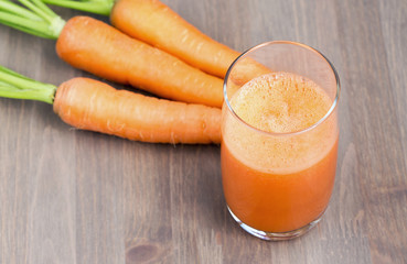 A glass of healthy carrot smoothie with carrots on wooden background. Selective focus