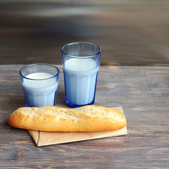 Jug of milk, glass of milk and bread roll on a wooden table. Special light.