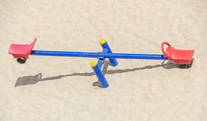 Teeter totter with red chairs, beach sand, balance, close up