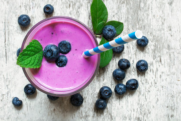 Blueberry smoothie in a glass with a straw and mint and fresh berries