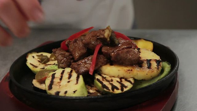 Chef garnishes hot meat dish, close up