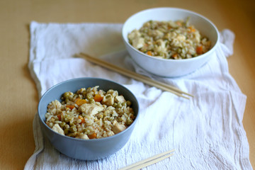 Fried rice with chicken and various vegetables, in two bowls with chopsticks. Selective focus.