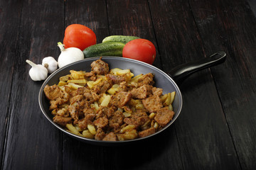 fried meat and potato with vegetables on wooden background