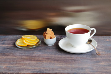 Fototapeta na wymiar A cup of tea, sugar and lemon slices on a wooden table against steel kitchen background with reflections 