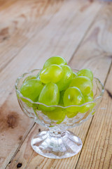 Green grapes in the crystal glass bowl on the wooden background