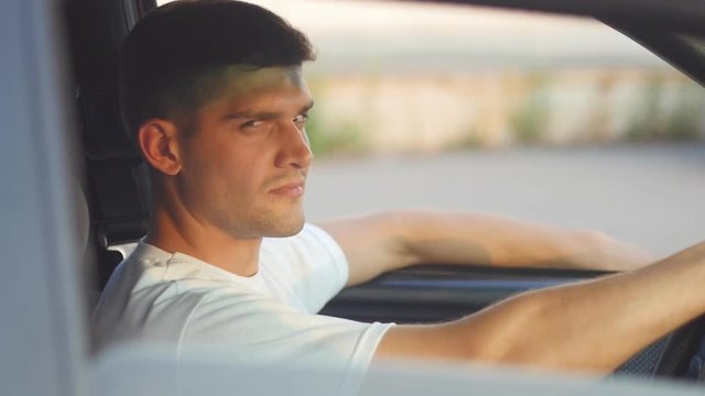 portrait of a young man behing the wheel looks at camera, slow-motion
