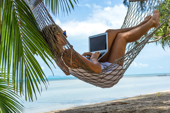 Young woman with a laptop in a hammock on the beach
