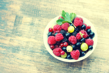 Fresh juicy berries, raspberries, currants, blackberries, a gooseberry in an white plate on a wooden surface