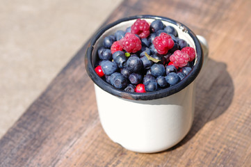 Juicy mature berries of raspberry and bilberry  in an iron mug on a wooden surface.